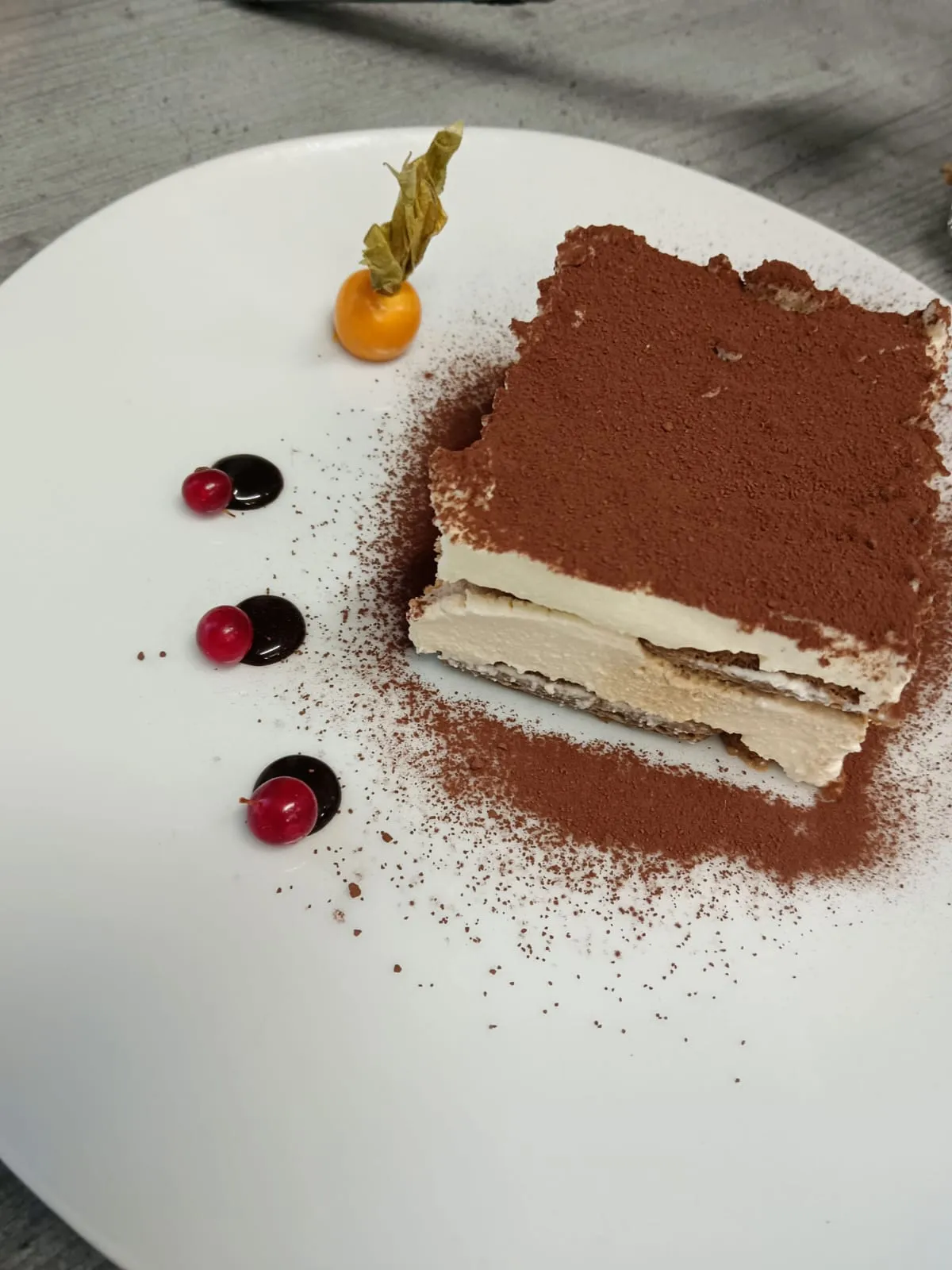 Hausgemachtes Tiramisu mit Kakaopulver, Beeren-Coulis und Physalis